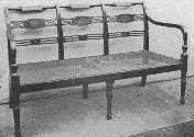 A three-chair settee of the Sheraton period, lacquered,
and with cane seat. It would be appropriate for a living-room or hall.