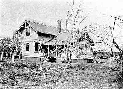 Two story frame house with gables and one story ell; two chimneys; picket fence.