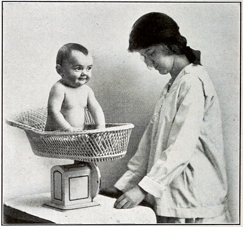 A baby in a basket on a scale
that is being read by a woman
