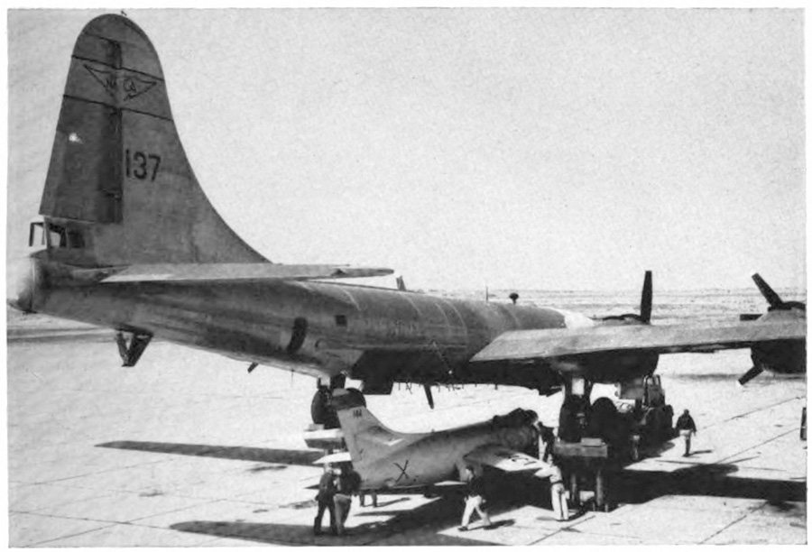 A crew attaching a small plane to the underside of a larger plane