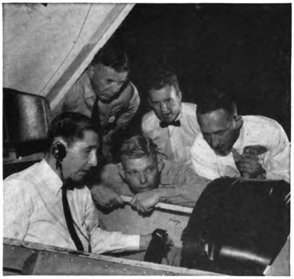 A goupf of men watching another manage controls