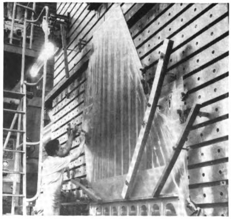 A worker standing in front of a wing lined up vertically near a wall